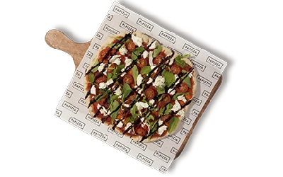 Pinsa con masa artesana ligera, crujiente y digestiva, con más de 72h de fermentación, Base de salsa de tomate, mozzarella bocconcin, rúcula selvática, tomate cherry y rulo de queso de cabra, finalizada con crema de vinagre balsámico.